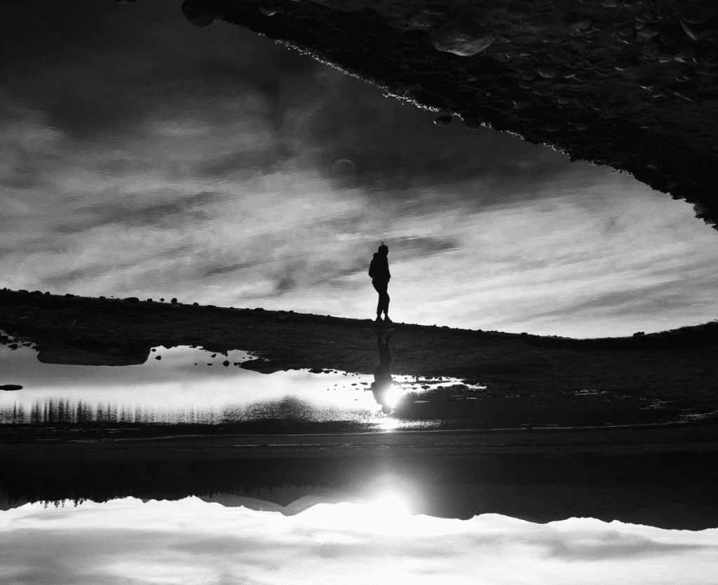 Black and white image for Arc'tyrex of a person walking on a bridge over a body of water.