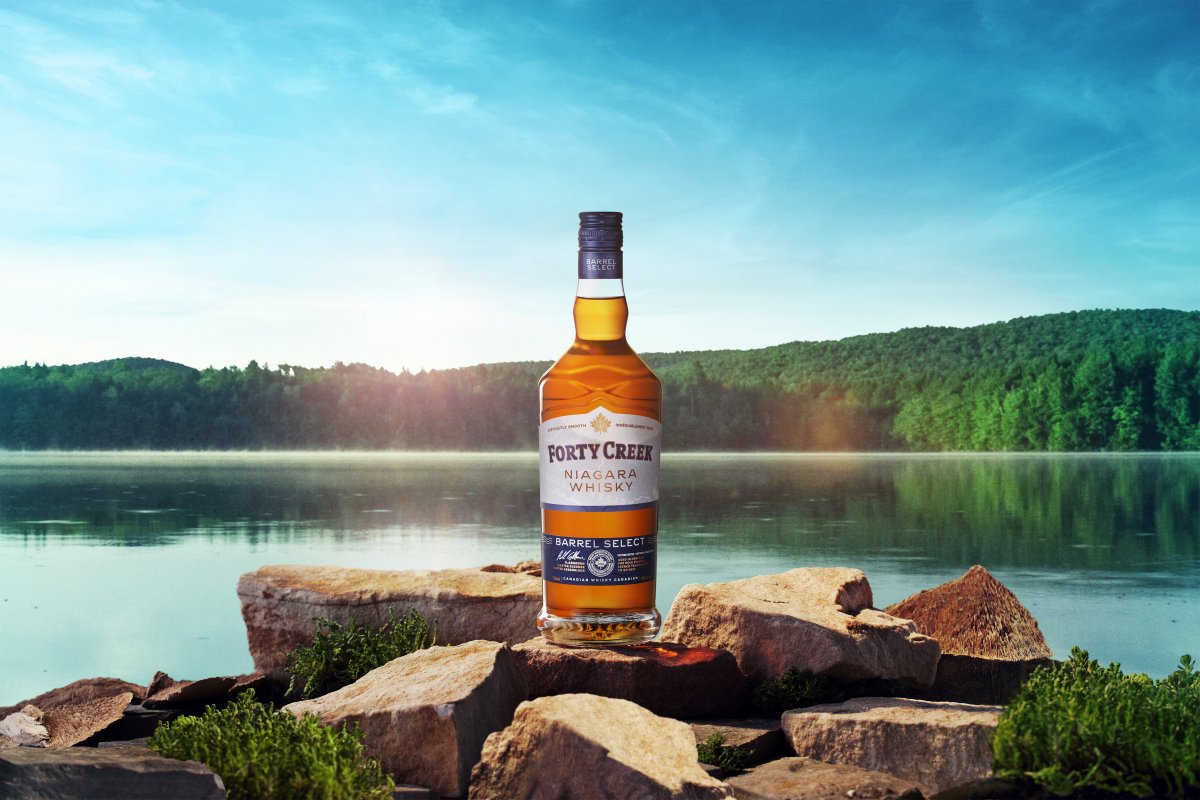 Bottle of Forty Creek Whisky sits on a rock in front of a lake.