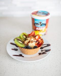 A waffle bowl with Neale's Sweet N' Nice Ice Cream, kiwis, strawberries, and blueberries in it.