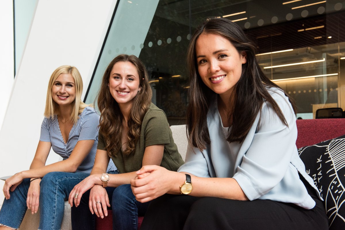 Roslyn McLarty, Ellen Hyslop, and Jacie deHoop, Co-Founders of The Gist, sit on a couch and smile at the camera