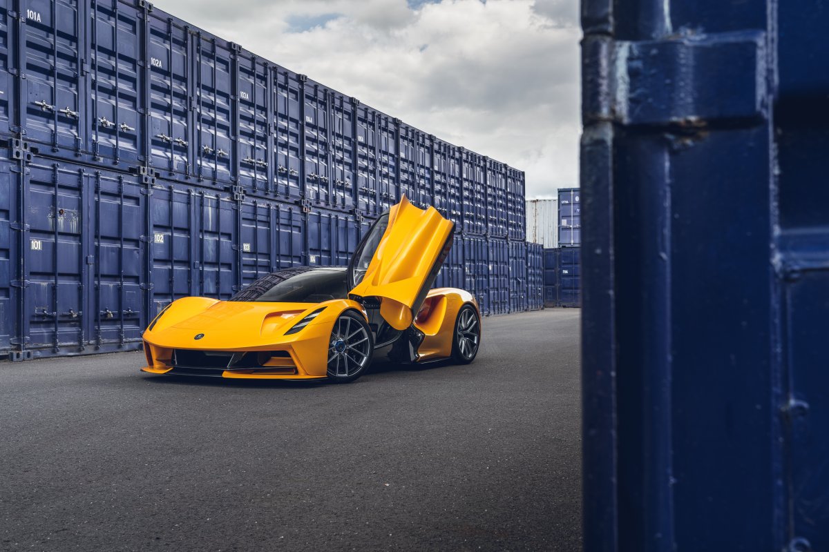 Bright yellow lotus evija in front of blue shipping containers