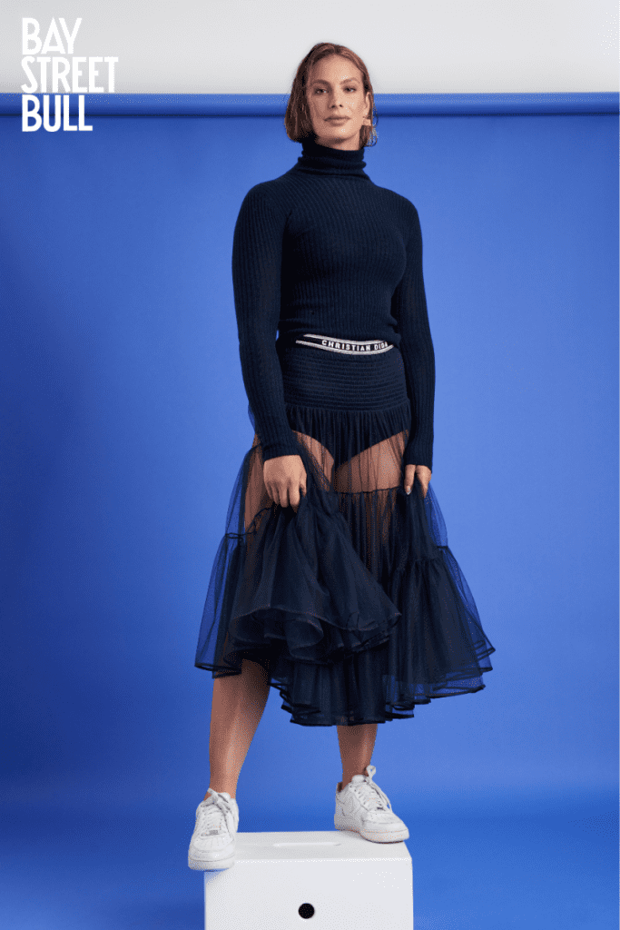 Penny Oleksiak standing on apple box in navy blue turtleneck and skirt against blue background