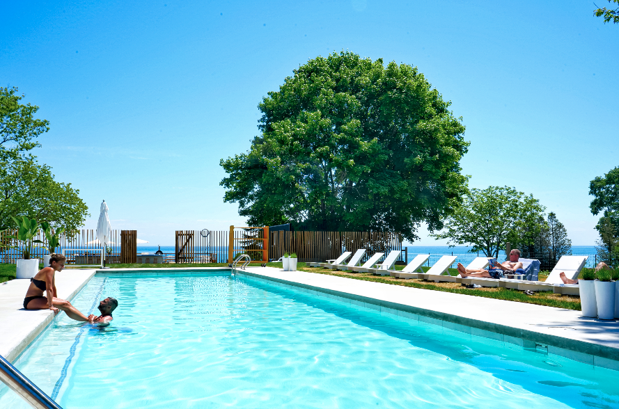 Motel poolside with two people swimming and lake in the background