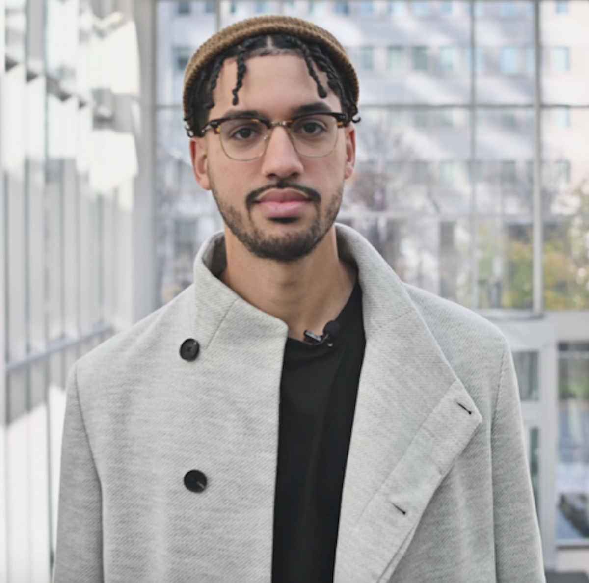 A Black man with a beanie hat and glasses, wearing a grey plaid coat stares at the camera. He is Phil G. Joseph, creator of Rep Matters.
