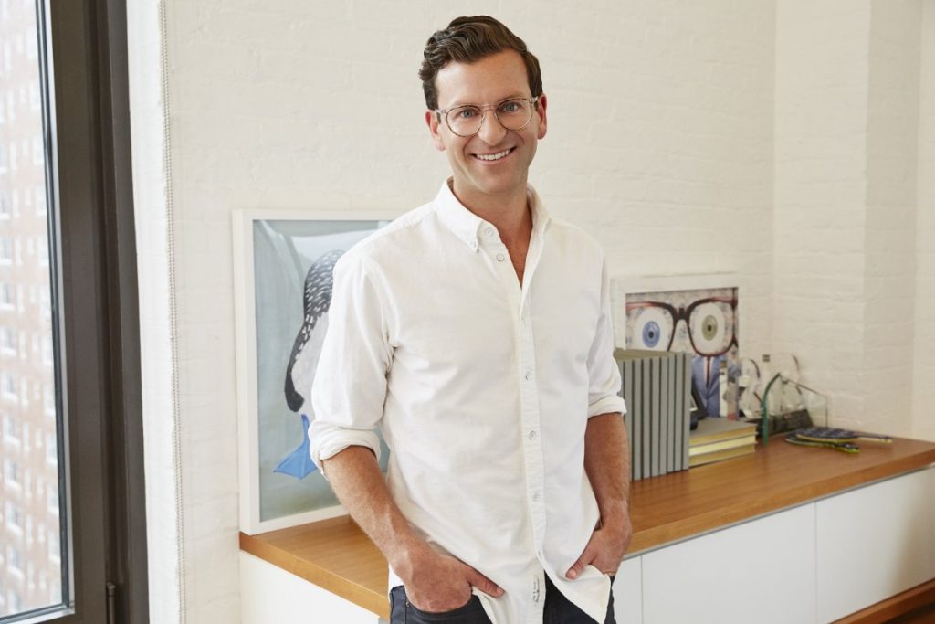 David Gilboa smiling wearing a white button up shirt leaning against counter