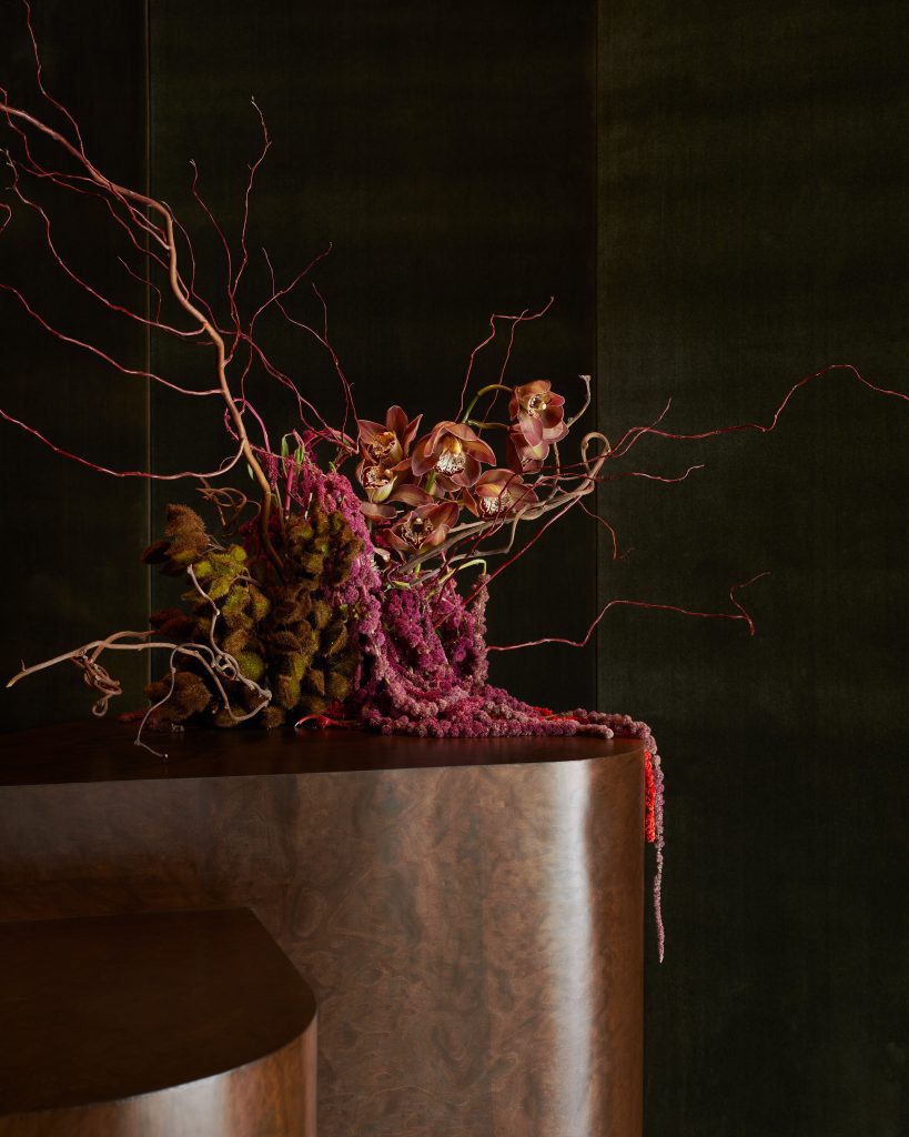 Overflowing floral arrangement spilling over marble countertop against dark wood backdrop.