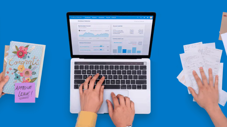 Apple laptop with spreadsheets and graphs on the screen. There are two hands resting on the keyboard. To the right is a stack of papers with a hand clutching them. To the left is a birthday card against a blue background.