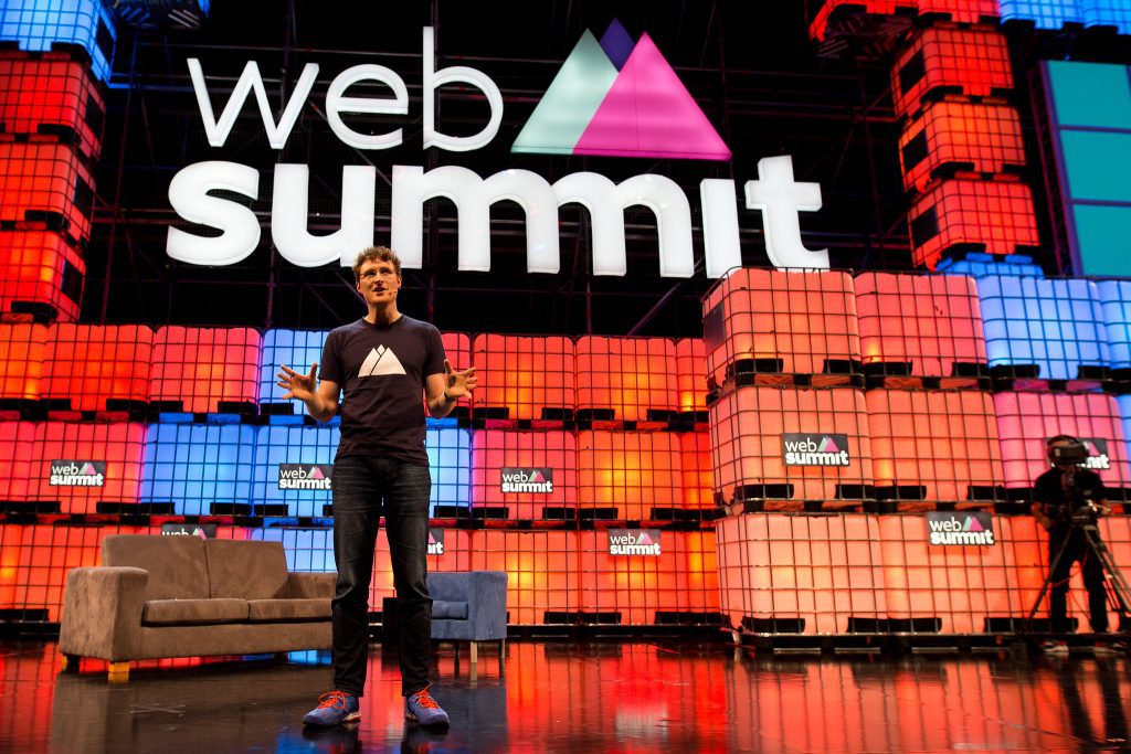 Paddy Cosgrave standing on stage at Web Summit conference. Behind him is a stage that is lit up with colourful blocks.