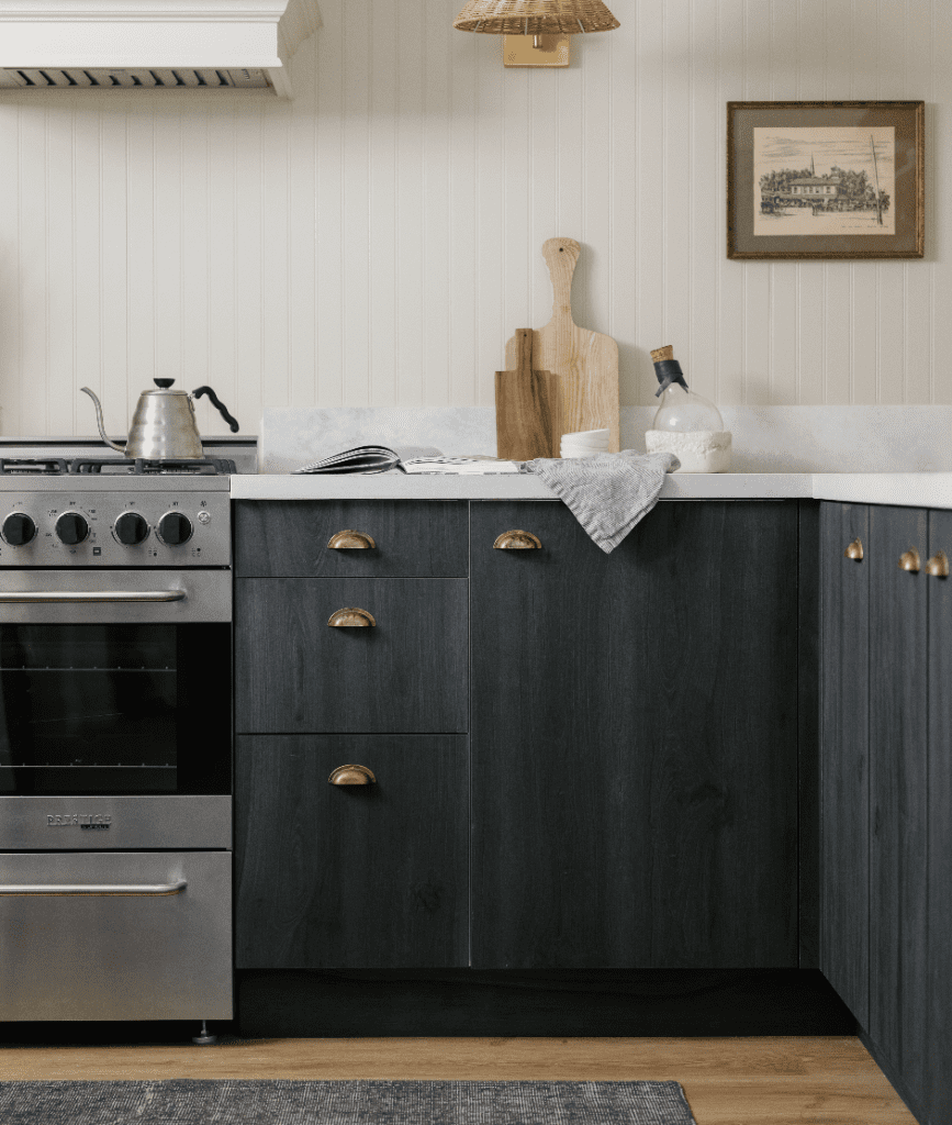 Kitchen corner with beige walls and assorted items on the countertop. There is a gas range and dark wood cabinets with brass handles.