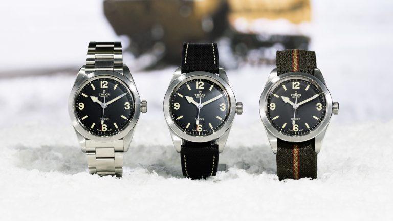 Three Tudor watches set on ice. One has a steel bracelet, the middle watch has a black strap, and the right watch has a khaki green strap. All of them have black faces.
