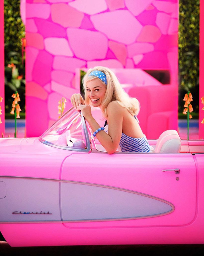 Barbie in a bright pink car. She is smiling at the camera.