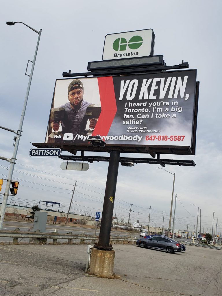 Photo of a billboard with a picture of Kevin heart on it. It says "Yo Kevin, I heard you're in Toronto. I'm a big fan. Can I take a selfie?"