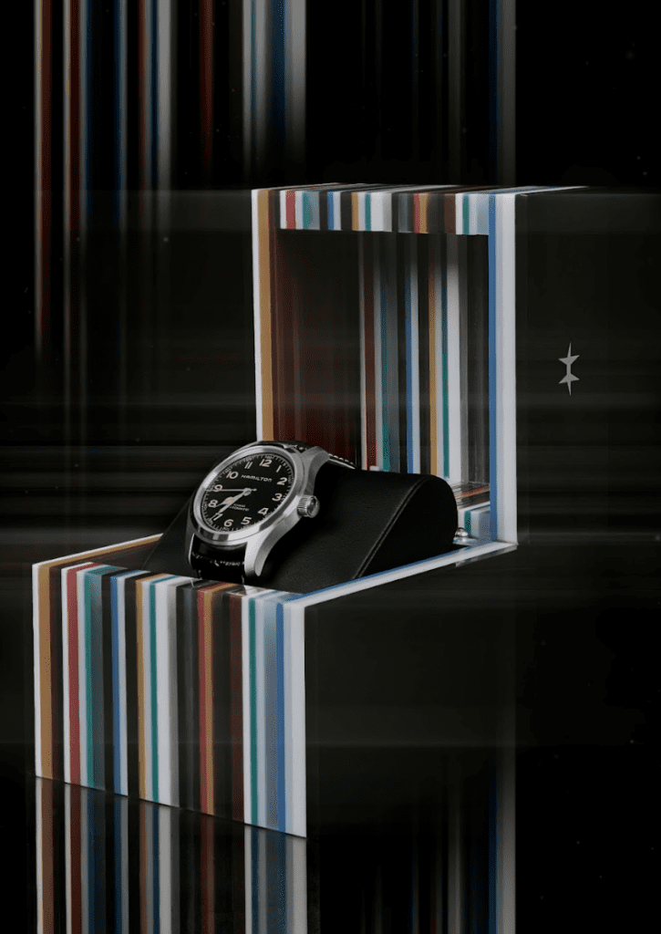A Hamilton watch with a black leather strap and silver case sits in a box with multicoloured linear lines.