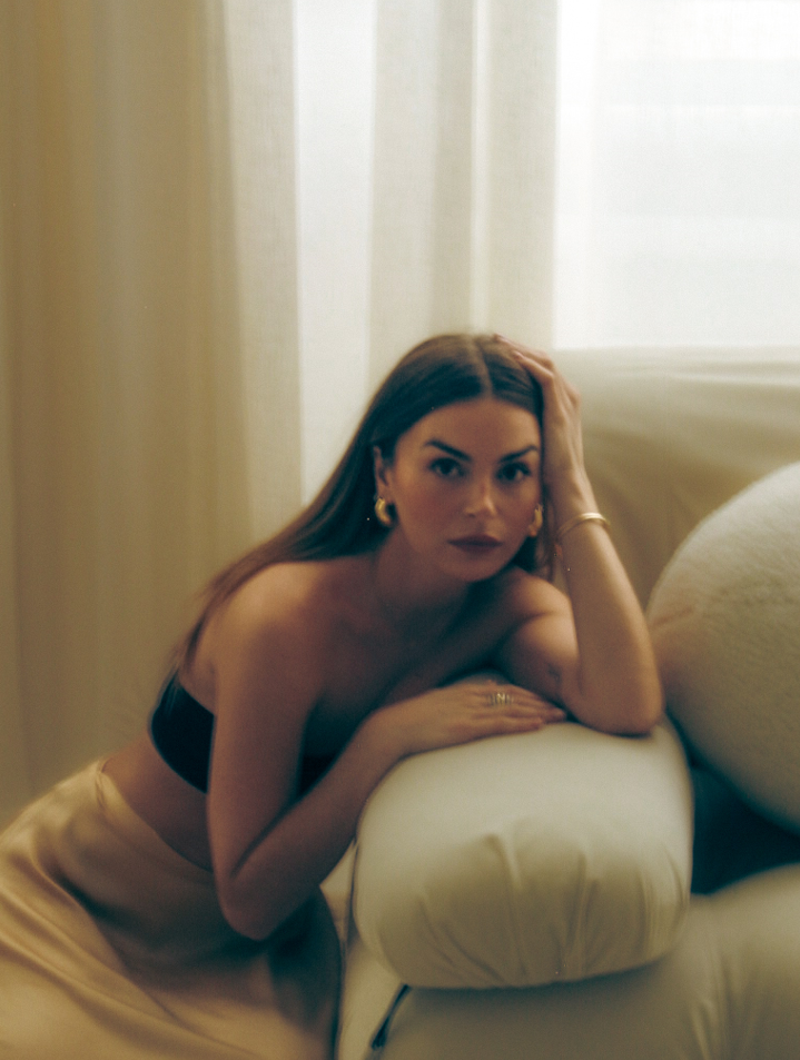 Photo of Allegra Shaw posed over the arm of a couch. She is looking at the camera.