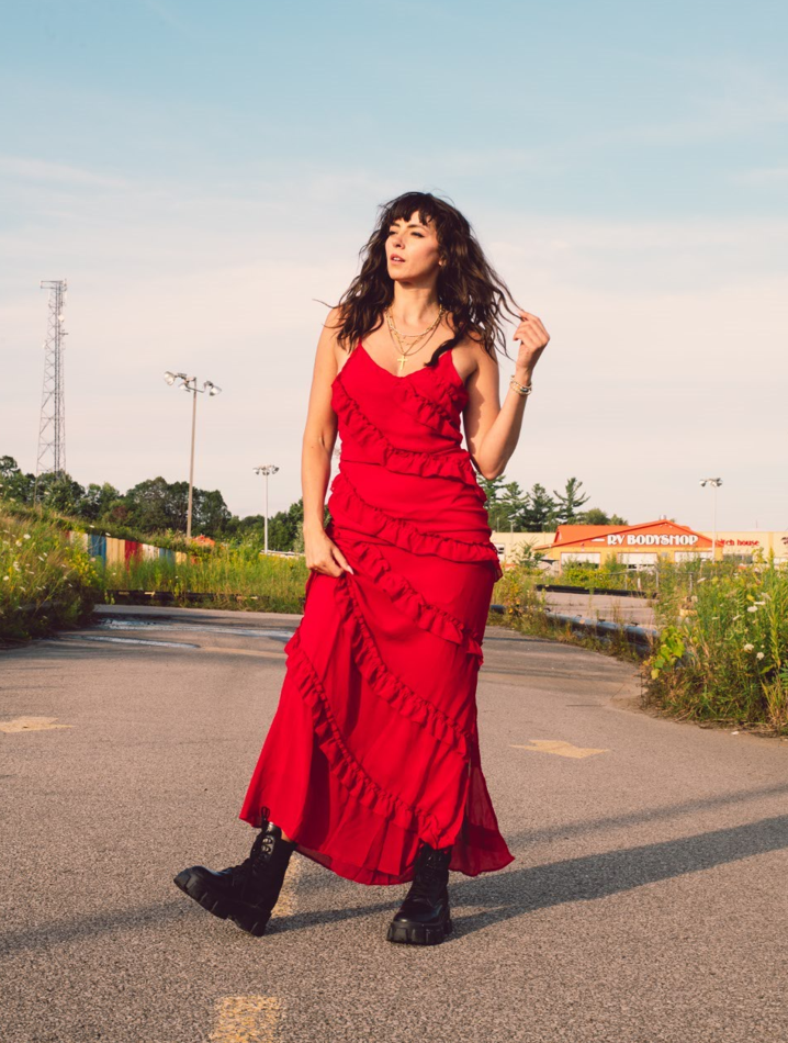 Photo of Briony Douglas standing in the middle of a road. She is wearing a red dress and black boots.