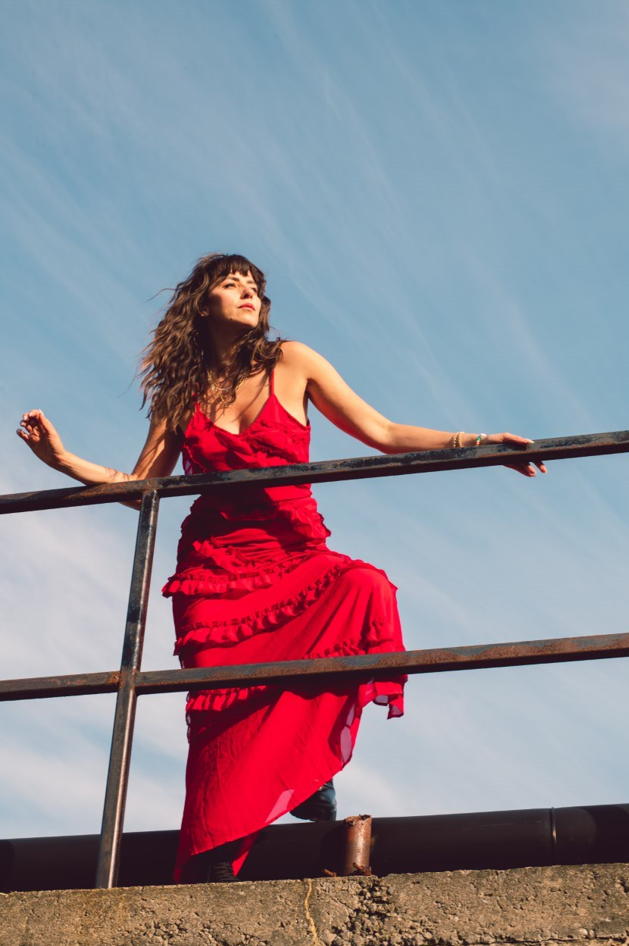 In this photo, a women is photographed from below. She is leaning against a railing and looking off into the distance.