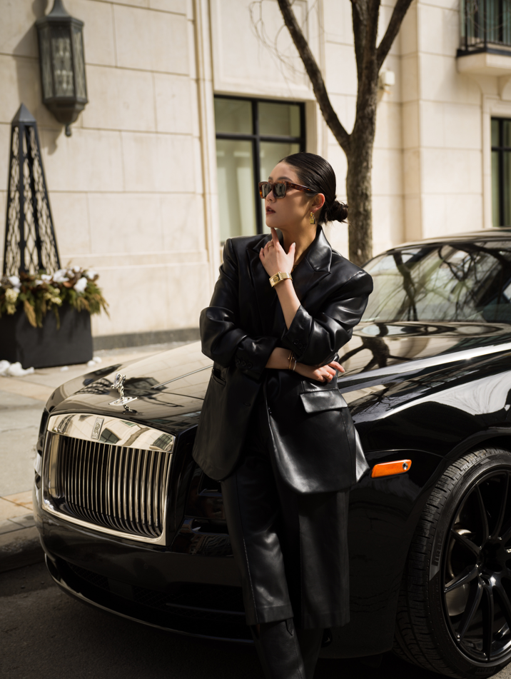 Photo of women wearing all black with black sunglasses posing in front of a black Rolls Royce.