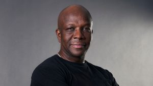 Donovan Bailey against a grey background and black t-shirt looking into the camera.