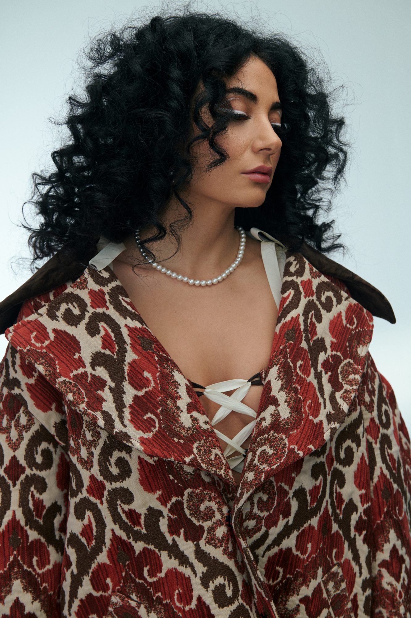 Dorian Who is looking down. Her hair is full of curls and she is wearing a large overcoat.