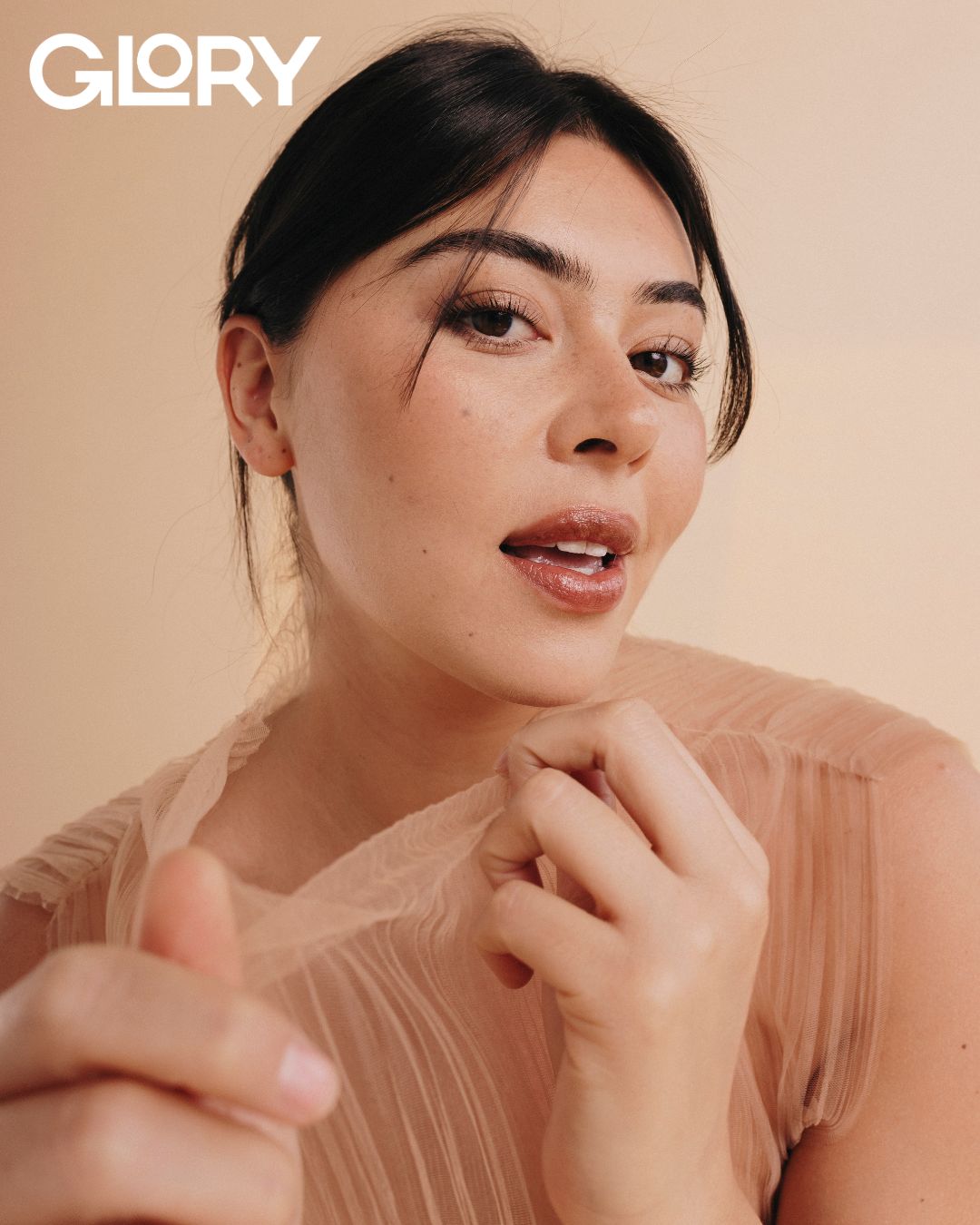 Portrait image of Lauren Chan looking into the camera. Her hair is pulled back and her bangs are framing her face. Her lips are slightly open and she is pulling the collar of her tunic towards the camera.