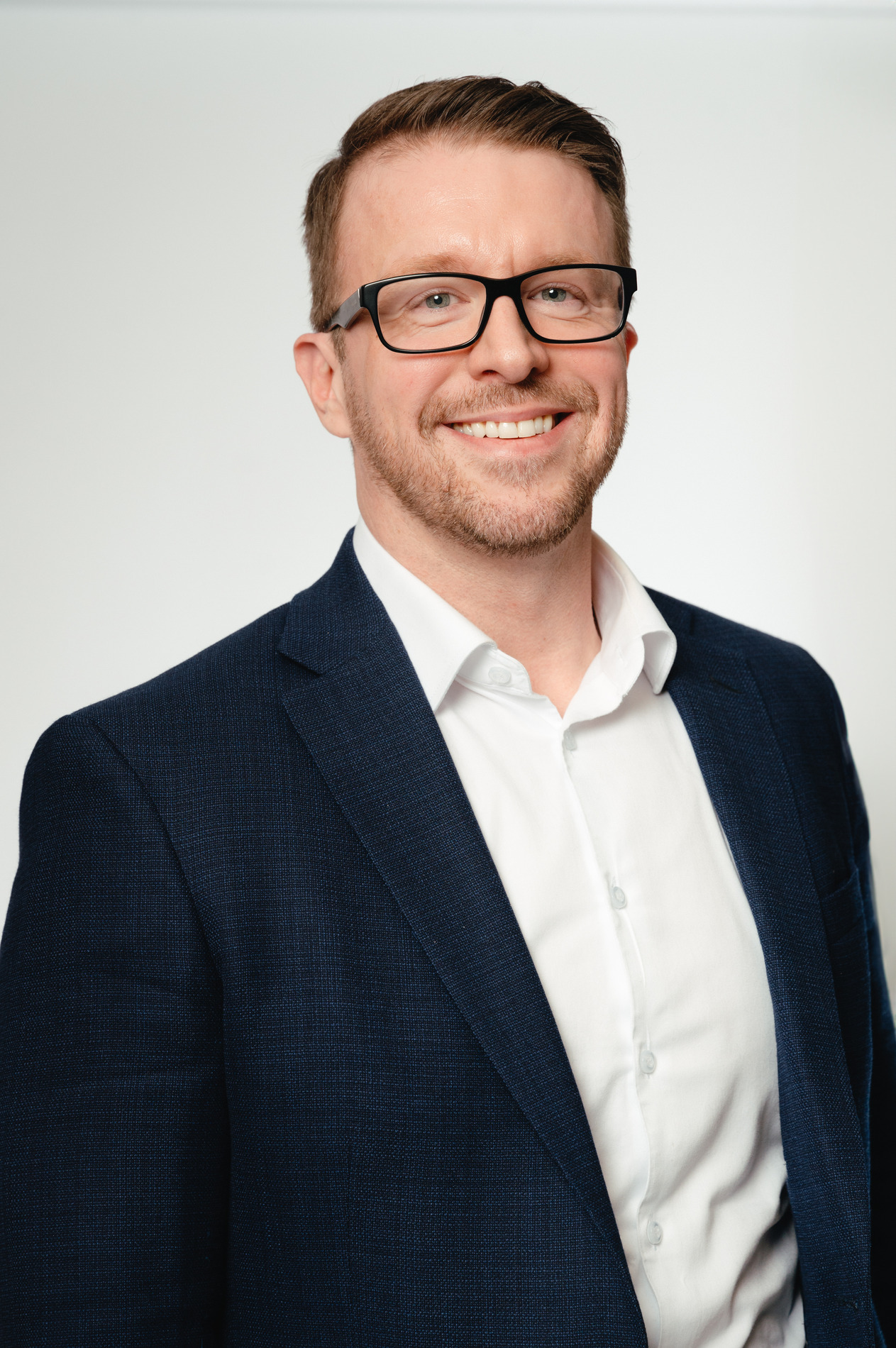 Shawn Stewart in a white button up shirt and navy jacket smiling against a white background.