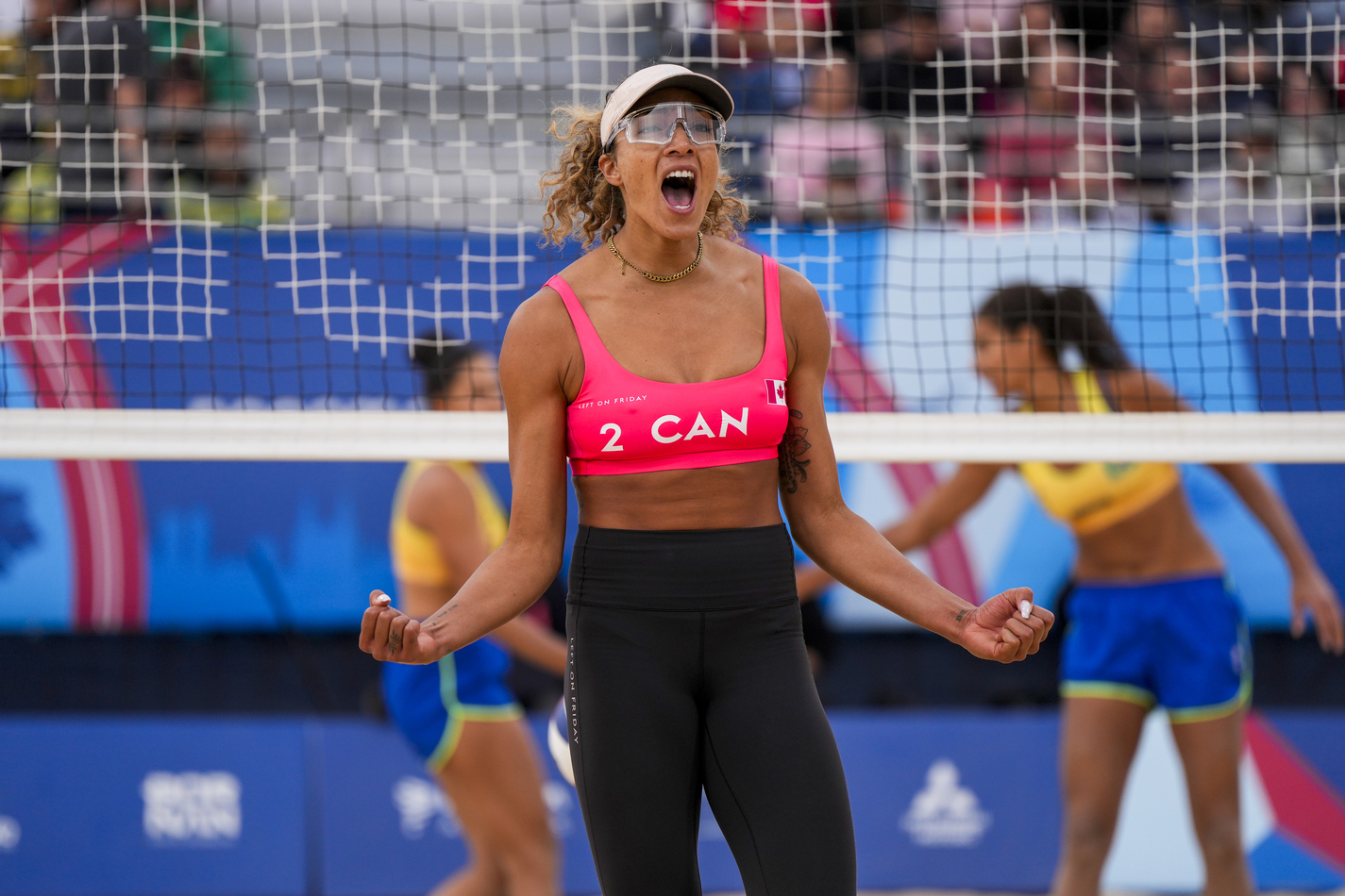 Brandie Wilkerson on a beach volleyball court. She is in front of a volleyball net looking victorious.