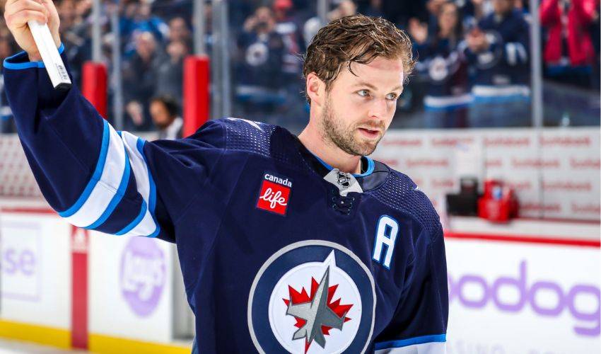 Josh Morrissey wearing a navy blue hockey uniform of the Winnipeg Jets at a hockey arena.