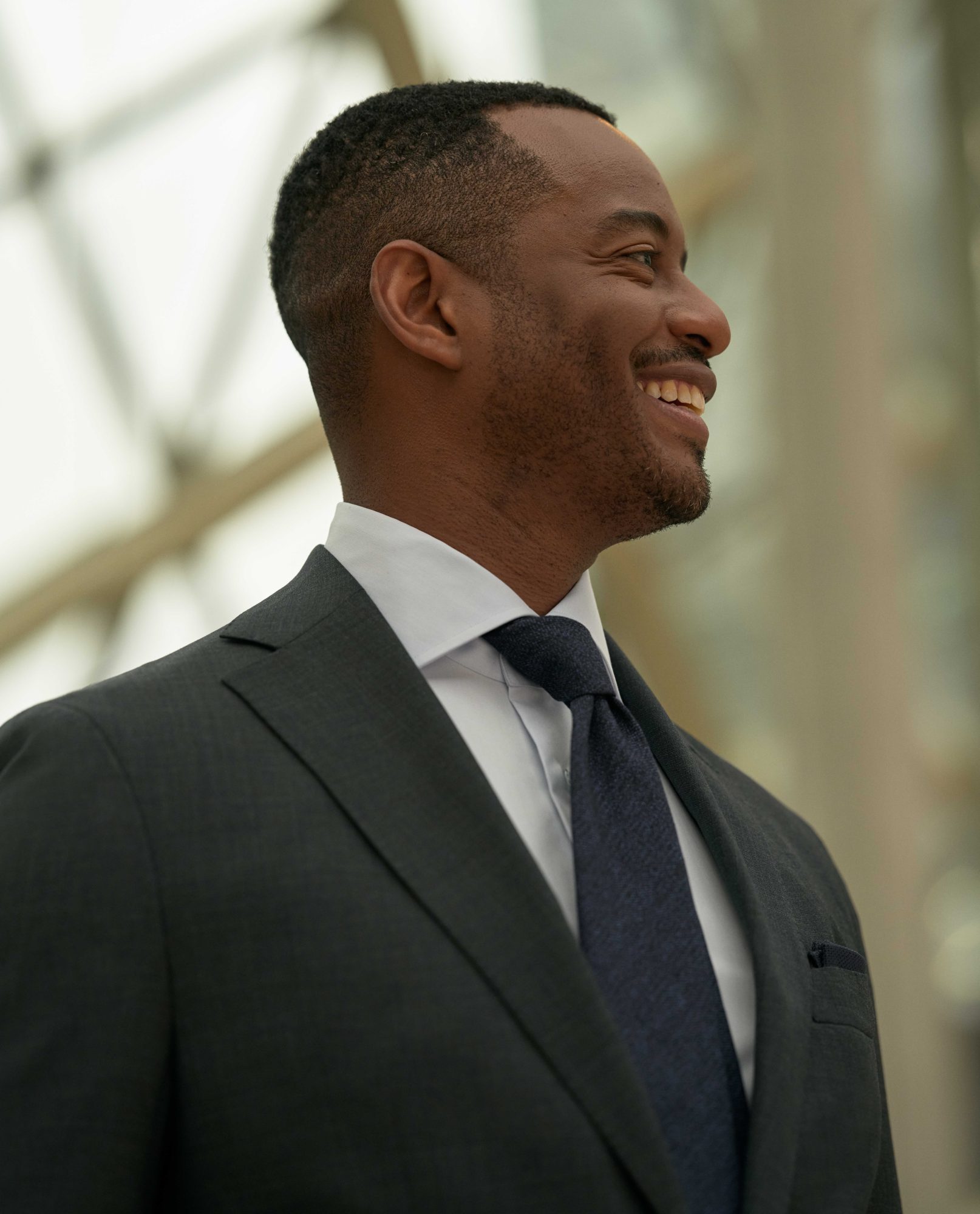 Portrait of Toronto Symphony Orchestra CEO Mark Williams smiling and looking off to the side in a charcoal grey suit and tie with white shirt.