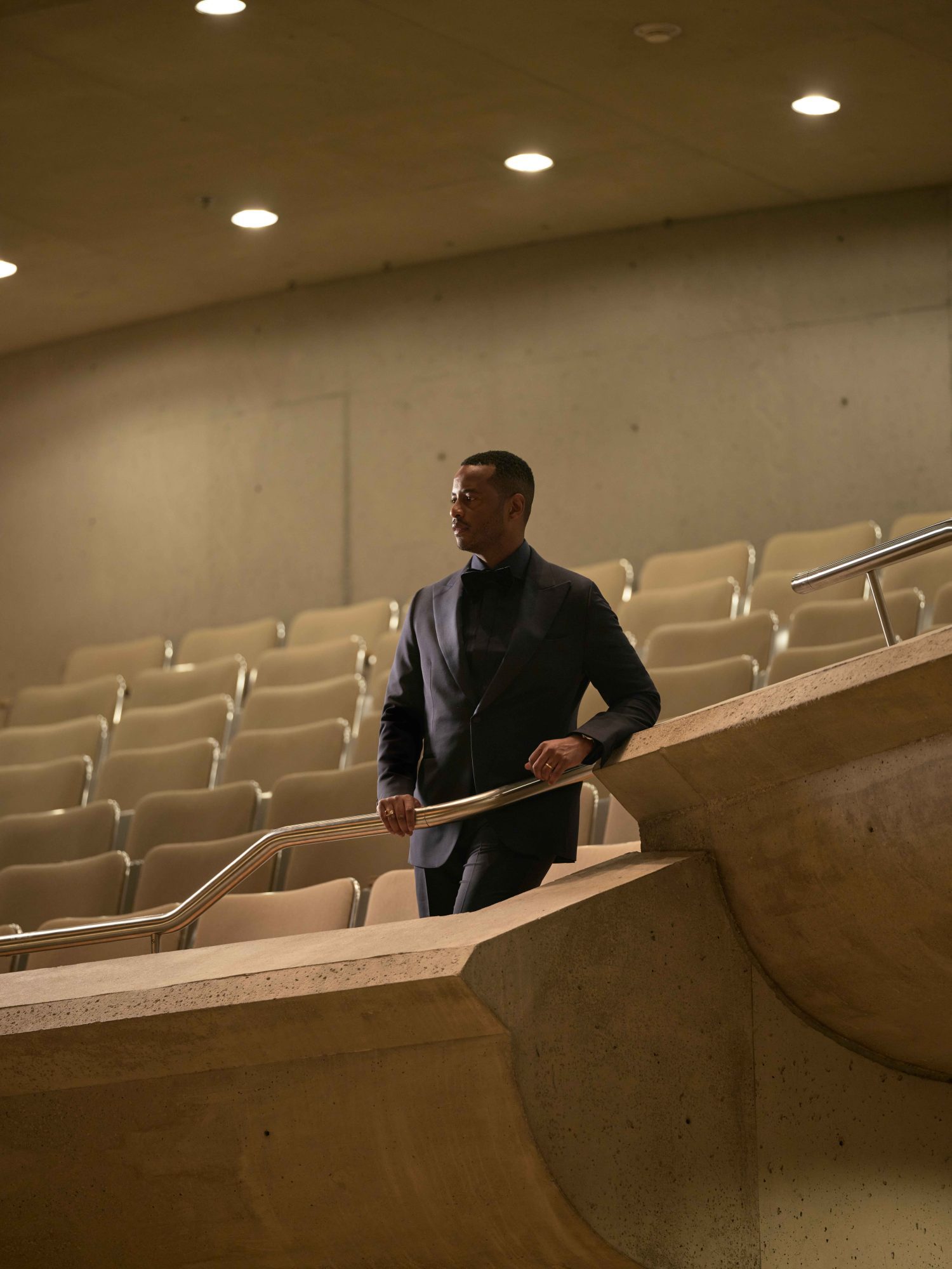 Toronto Symphony Orchestra CEO Mark Williams in an all-black suit standing on balcony of the auditorium grasping the rail and looking down.