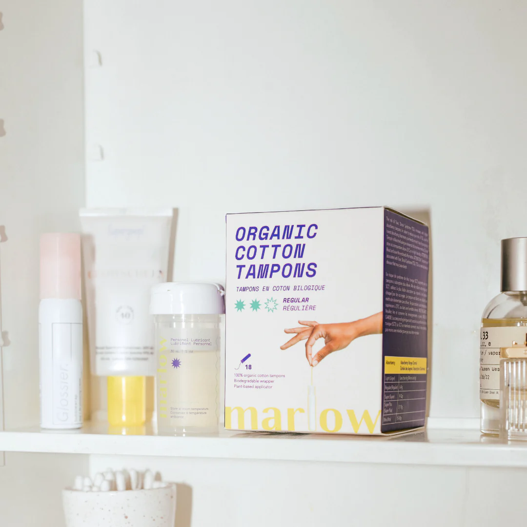 Bathroom shelf with multiple beauty products and a box of Marlow tampons that say "Organic cotton tampons" on the cover.