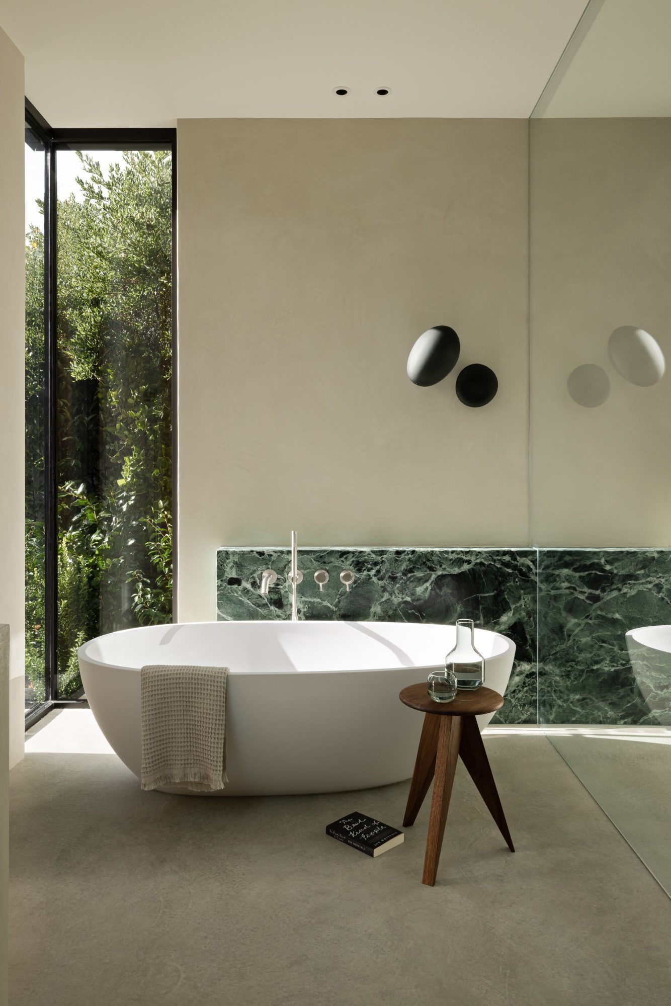 Minimalist and serene bathroom with a soaker tub and wooden stool. The windows face a bunch of foliage.