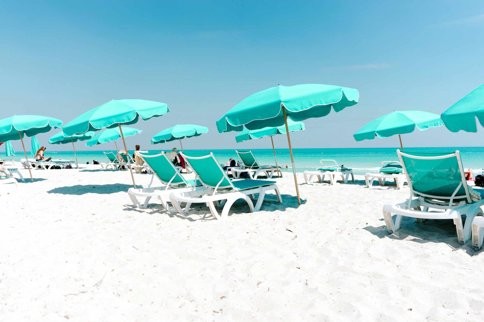 A sunny beach filled with Tiffany-blue beach chairs and umbrellas facing towards the ocean.