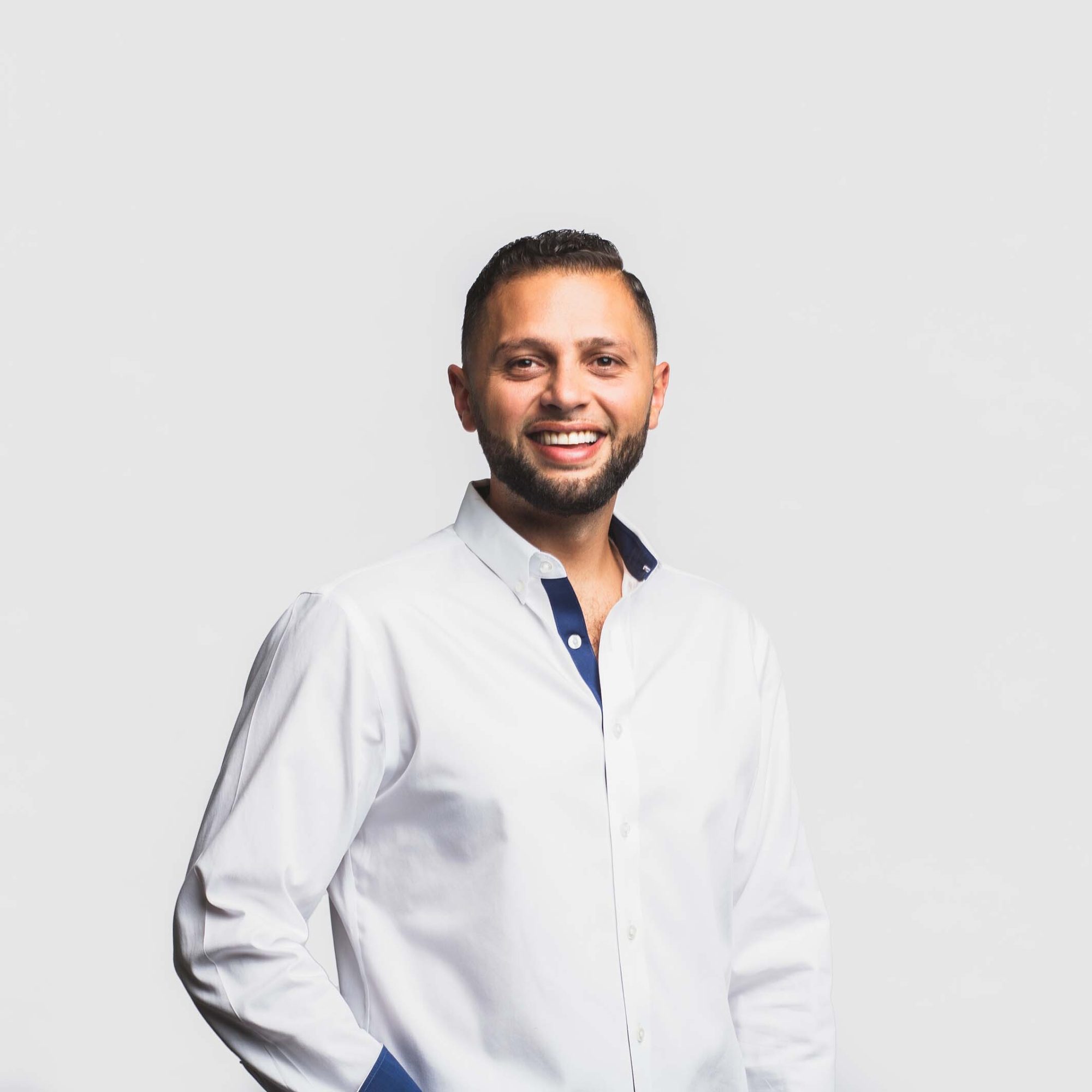 Abdullah Snobar standing in a white shirt and smiling into the camera against a white background.