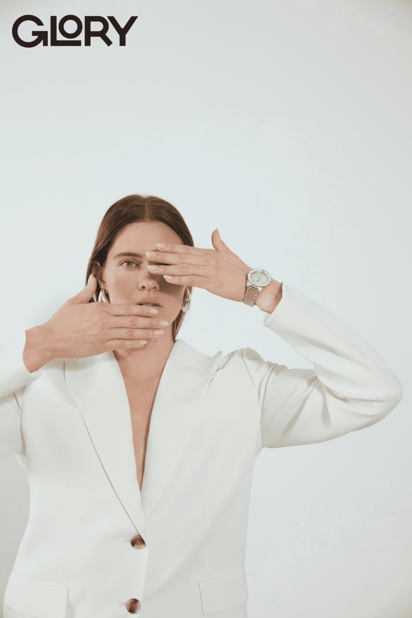 Alysha Newman wearing a white blazer. Her arms are raised. One is covering her left eye and the other is covering her mouth. She is wearing a Rado watch.