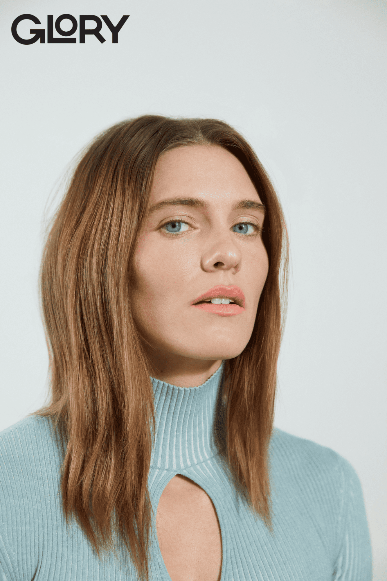 Portrait of Alysha Newman wearing a light blue knitted tunic with a keyhole cutout. Her hair is brown and she has striking blue eyes.