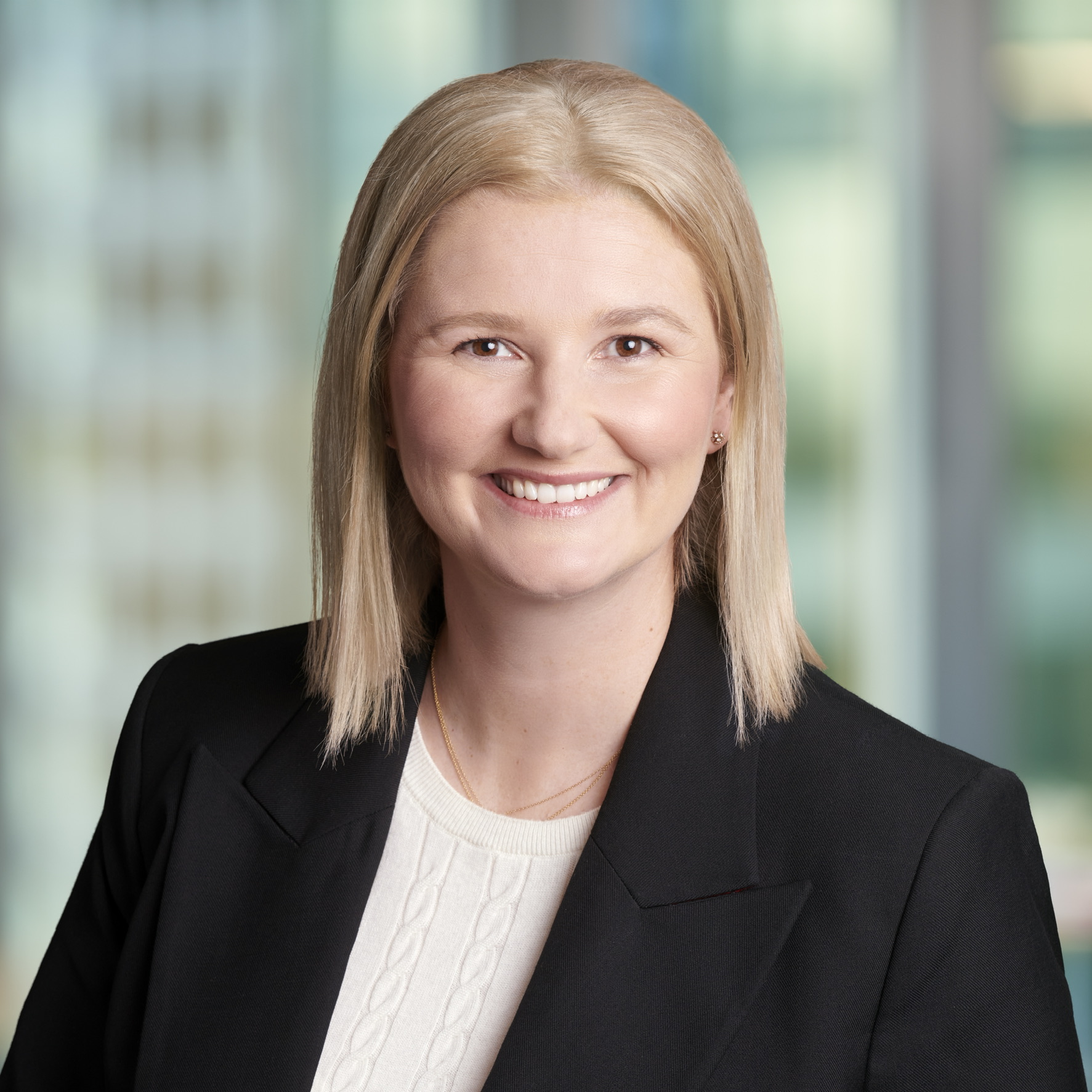 Daria Hill headshot wearing a black blazer and white shirt. She has shoulder-length blond hair and is smiling into the camera with a cityscape in the background.