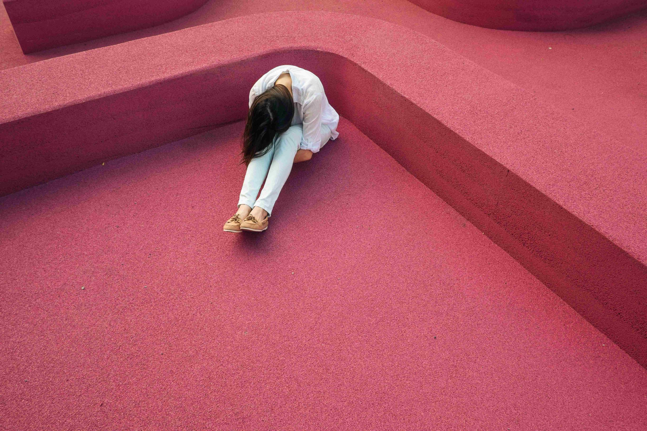 A woman wearing all-white hunched over into her knees sitting on a pink floor.