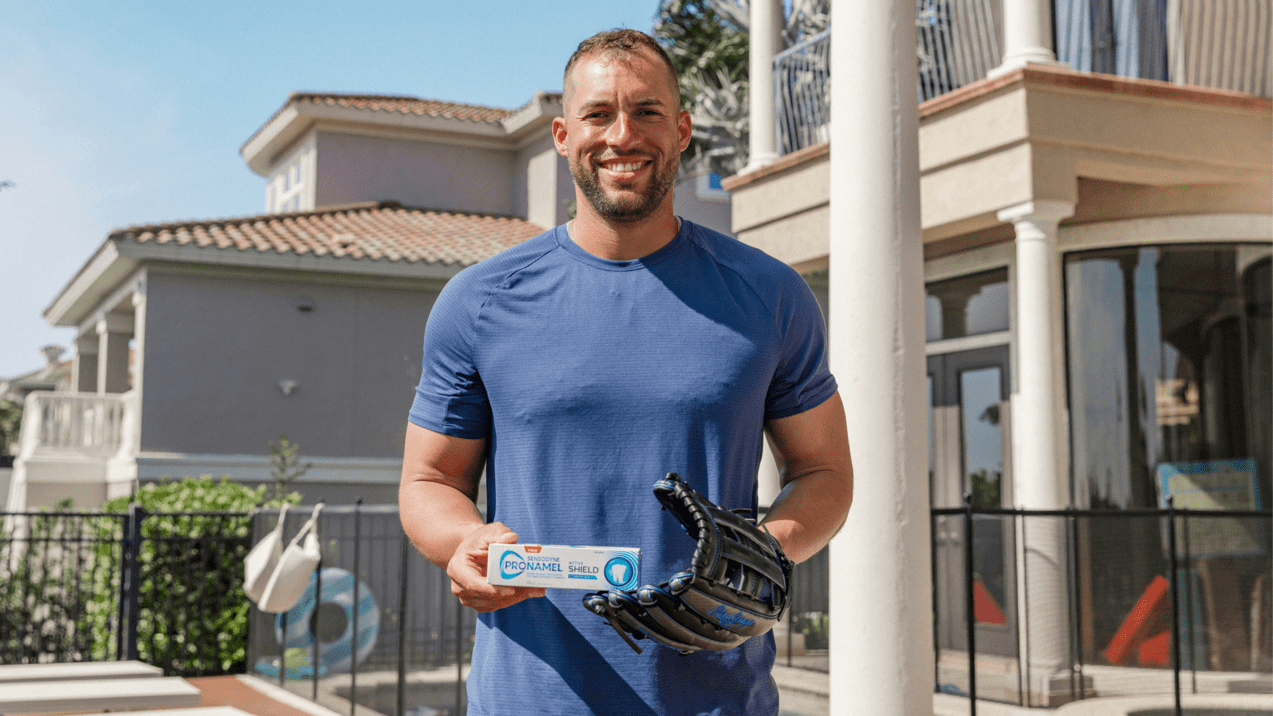 George Springer wearing a blue t-shirt, smiling and holding a pronamel toothpaste package.